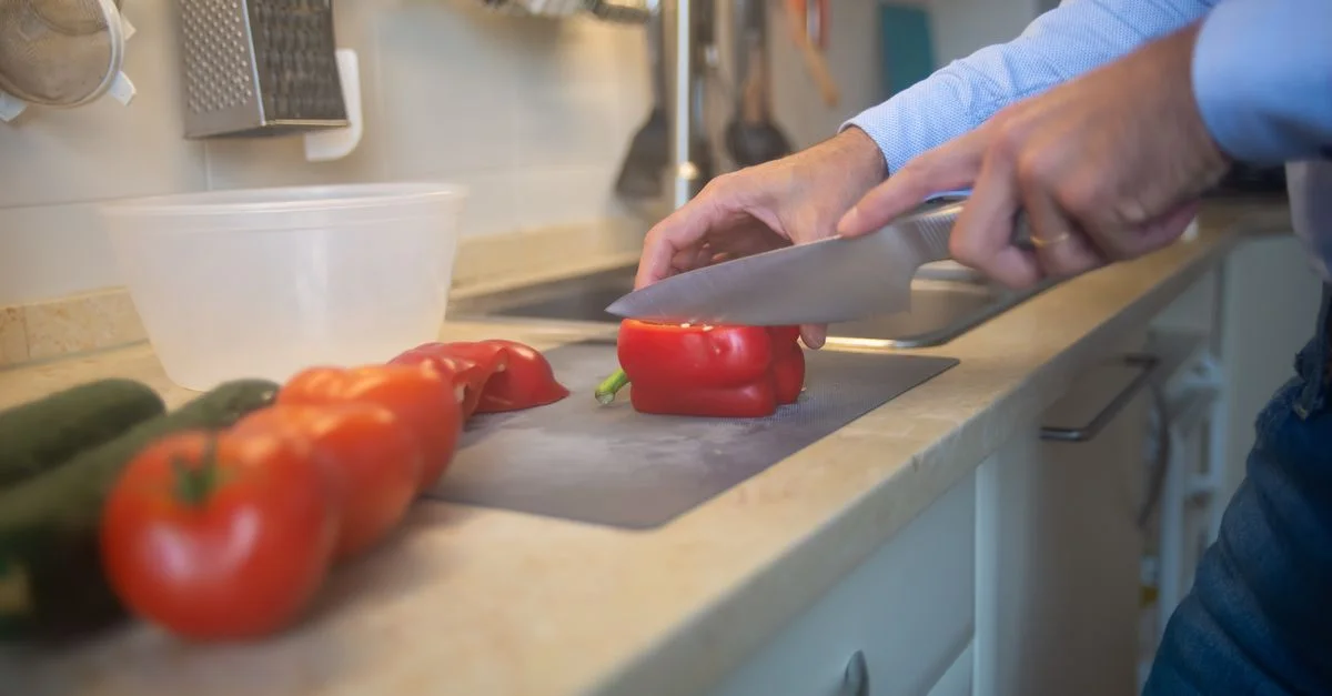 Un homme tranche des poivrons rouges et des tomates sur un comptoir de cuisine avec un couteau.