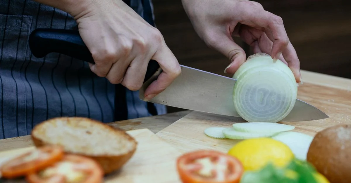 Gros plan sur des mains tranchant des oignons avec des légumes frais sur une planche à découper.