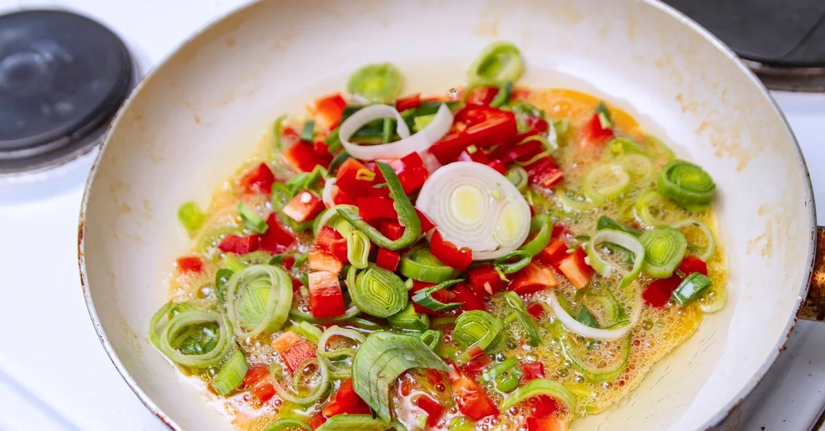 Des légumes colorés cuisent dans de l'huile sur une cuisinière.