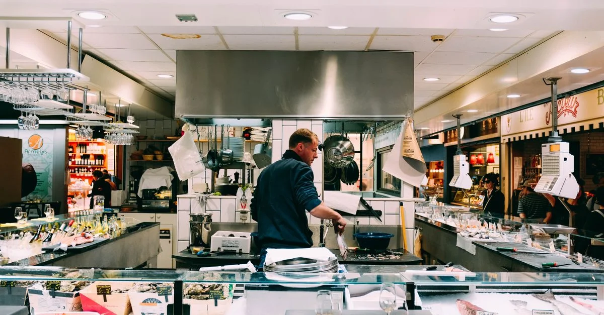 Un chef prépare des fruits de mer frais à vendre dans un marché intérieur, entouré d'ingrédients et d'expositions.